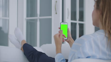 Woman-using-for-video-call-mobile-phone-vertical-green-screen.-Female-holding-in-hand-portable-gadget-close-up-indoors-home-living-room.-Mock-up-for-tracking-or-watching-content.